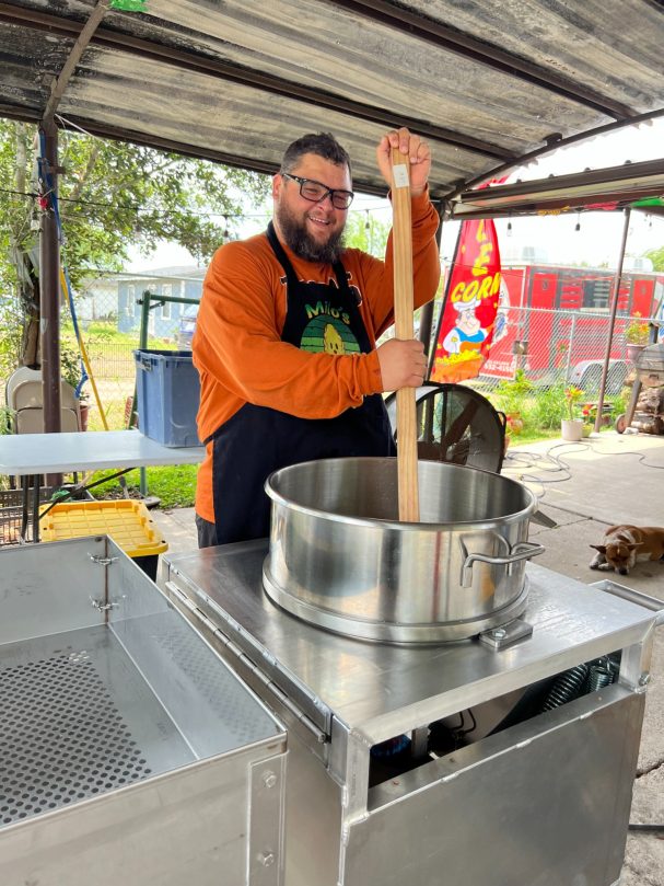 A person stirring a large pot on a stove in an outdoor cooking area.